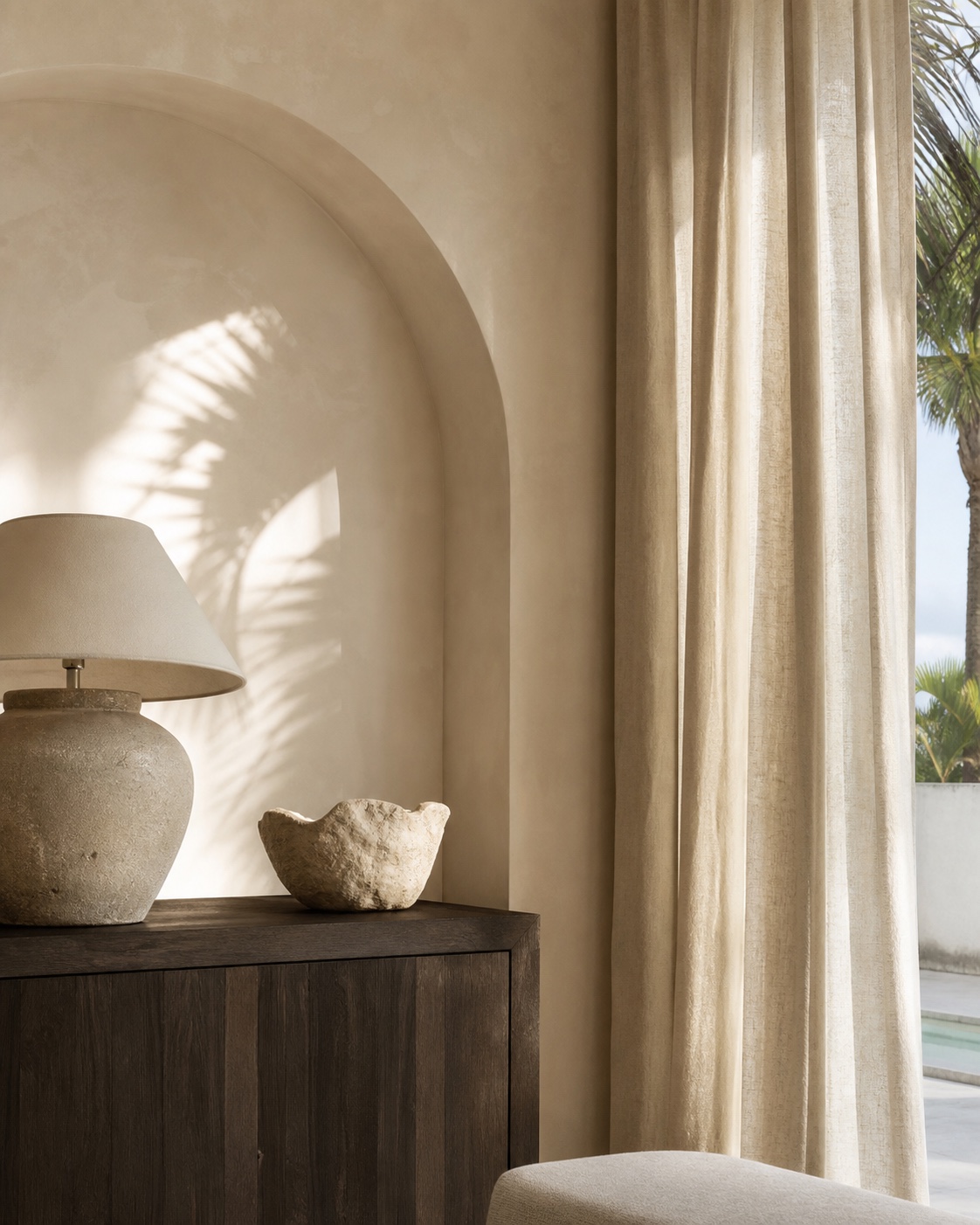A quiet interior detail with a plaster arch, stone lamp, linen drapery, and afternoon light.